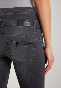 Tmavě šedé džíny z denimu s přiléhavým střihem. Mezi funkce patří zadní kapsa, značková visačka a jemné vyblednutí. Hladká textura s detaily prošívání.