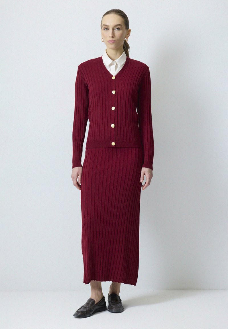 Bordeaux ribbel gebreide cardigan met gouden knopen en een bijpassende midi-rok. Kenmerken zijn een V-hals, een slim fit, textuurstof en een rechte zoom.