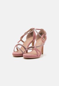 Sandales à talons hauts en daim rose avec des brides croisées, ornées de détails argentés et d'une semelle intérieure rembourrée pour le confort.