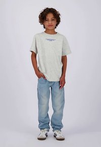 Lichtgrijs t-shirt met korte mouwen en blauwe tekst, gecombineerd met lichtblauwe cargobroek en witte sneakers met donkere accenten.