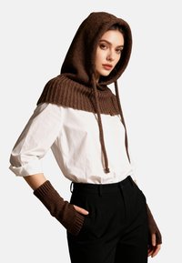 Fular cu glugă tricotat, de culoare maro, cu un design cu nervuri, asortat cu mănuși fără degete. Modelul poartă o cămașă albă și pantaloni negri.