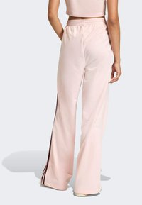 Jasnoróżowe spodnie o szerokich nogawkach wykonane z gładkiej tkaniny, z kontrastowym brązowym paskiem po bokach i elastycznym pasem.