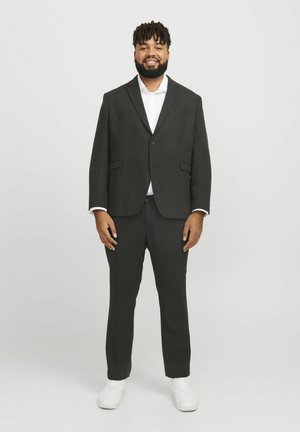 Dunkelgrauer Anzug mit einem maßgeschneiderten Blazer und passenden Hosen. Darunter ein weißes Hemd, kombiniert mit weißen Sneakers.