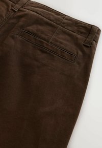 Brown corduroy pants showing the back waistband, belt loop, and single welt pocket with clean stitching detail.