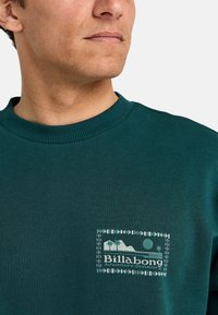 Zielona bawełniana bluza z ribbanym dekoltem i białym nadrukiem logo przedstawiającym góry i palmy na piersi.