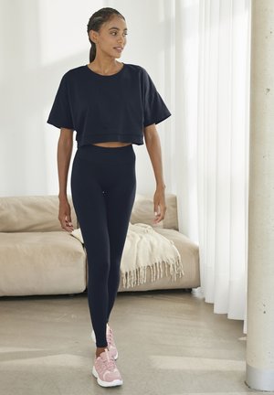 Marineblaues, kurzes T-Shirt, hochgeschnittene marineblaue Leggings und hellrosa Sportschuhe; flache, glatte Textur; lässiges Design. Innenraum.