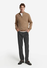 Hellbraunes langärmliges Pullover mit einem Viertel-Reißverschluss-Kragen, kombiniert mit dunkelgrauen Hosen und braunen Schuhen; glatte Textur, schlichte Gestaltung.