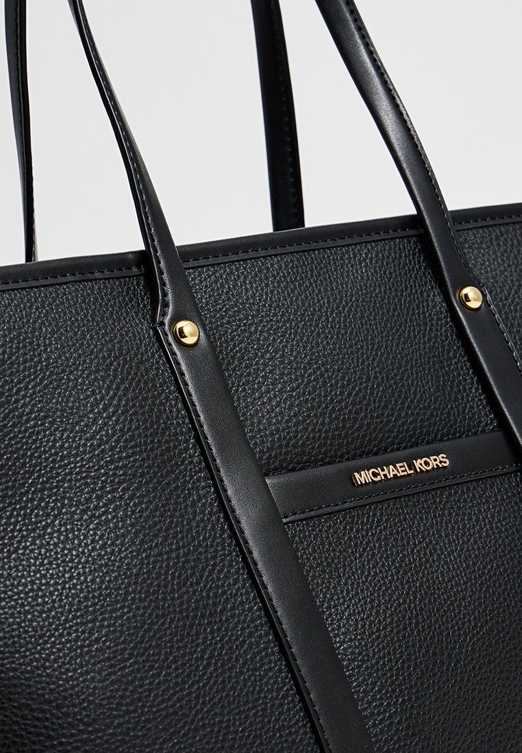 Schwarze Leder-Tote mit strukturiertem Finish, goldenen Hardware-Akzenten und einem prägierten Logo auf der Vorderseite. Verfügt über doppelte Schulterriemen.