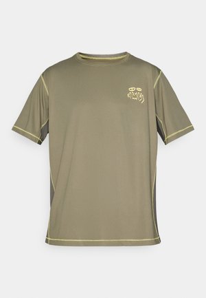 Alyvinės žalios spalvos trumpomis rankovėmis marškinėliai su geltonomis kontrastingomis siūlėmis ir maža grafine tekstine ženklinimu "KARMA" kairėje krūtinės pusėje.