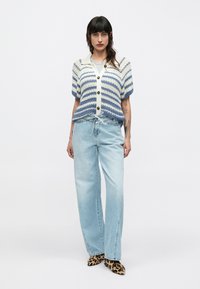 Cárdigan de punto con rayas azules y crema, mangas cortas abullonadas y botones en la parte delantera. Combinado con vaqueros de pierna ancha azul claro y zapatos con estampado animal.