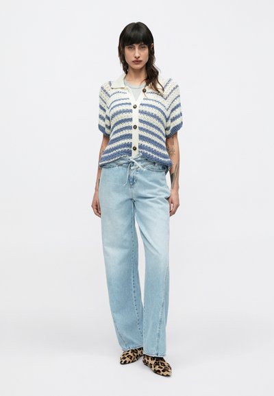 Πλεκτή ζακέτα με μπλε και κρεμ ρίγες, κοντά φουσκωτά μανίκια και κουμπιά μπροστά. Συνδυασμένη με ανοιχτό μπλε τζιν παντελόνι φαρδιάς γραμμής και παπούτσια με animal print.