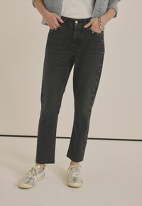 Sorte denim jeans med høj talje, lige ben og rå kanter. Har sølvfarvet knapudstyr og trykknapdetaljer langs sidesømmene.