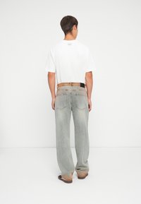 Witte t-shirt met korte mouwen gecombineerd met lichtgrijze wijde jeans, met een vervaagd uiterlijk en een tan-bruin leren tailleband. Zwarte riemaccent.