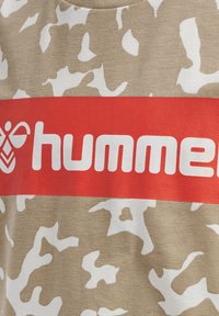 Camiseta sin mangas beige con un patrón de camuflaje blanco, adornada con una atrevida franja horizontal roja que muestra el texto "hummer" en blanco.