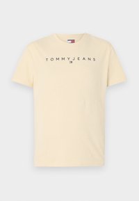 Kremowa bawełniana koszulka z krótkim rękawem, z logo "TOMMYJEANS" w ciemnoszarym kolorze na przodzie i małym akcentem logo.