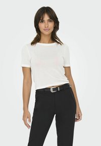 T-shirt bianco a maniche corte con scollo rotondo, abbinato a pantaloni neri con una fibbia decorativa argentata e una trama di tessuto liscia.