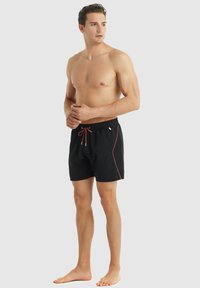 Pantaloni da bagno neri con cintura elastica e cordino rosso, dotati di una sottile linea di accento laterale e un design a taglio rilassato.