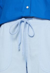 Pantalones cortos de algodón azul claro con una textura suave, que cuentan con una cinturilla ajustable y costuras visibles. Incluyen dos bolsillos laterales.