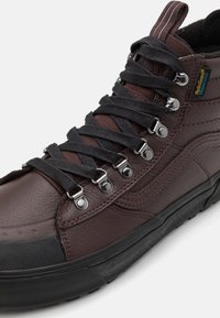 Brune lærhøye sneakers med svarte tekstil snørebånd, metallhull, teksturerte side mønstre og gummisåle. Vanntette materialer inkludert.