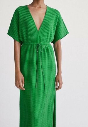 Groene maxi-jurk met textuur, diepe V-hals en korte mouwen, voorzien van een tailleband om te verstellen en een zijsplit voor bewegingsvrijheid.