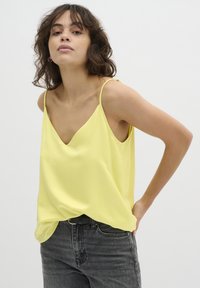 Camisole in satin giallo con scollatura a V e spalline sottili, abbinata a jeans in denim grigio scuro. Tessuto liscio, stile casual.
