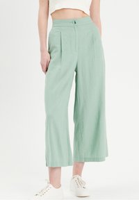 Pantalon à jambes larges vert clair avec plis à l'avant, taille haute, et fermeture par un seul bouton, fabriqué dans un tissu doux et texturé.