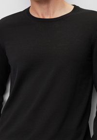 Schwarzes Langarmshirt aus einem glatten, leichten Stoff; mit einem klassischen Rundhalsausschnitt und dezenten Rippdetails am Kragen.