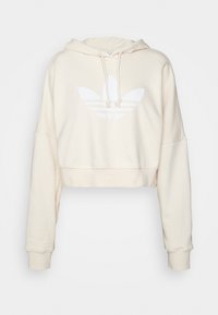 Zkrácená mikina v krémové barvě, s klokánkovou kapsou, kapucí na stahovací šňůrku a bílým logem adidas trefoil na přední straně. Měkká textura látky.