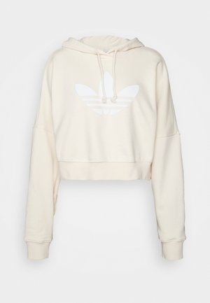 Cropped Hoodie in Creme mit Kängurutasche, Kapuze mit Kordelzug und einem weißen Adidas Trefoil-Logo auf der Vorderseite. Weicher Stoff.