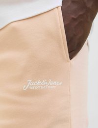 Svijetlo breskvasti jogger šortsevi napravljeni od teksturiranog materijala, sa bijelim otisnutim logotipom "Jack & Jones Essentials Dept." na bočnoj džepu.