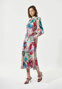 Midikleid mit Blumenmuster in mehreren Farben; hat einen hohen Ausschnitt, lange Ärmel, Taschen und eine fließende Silhouette. Getragen mit Riemchen-Heels.