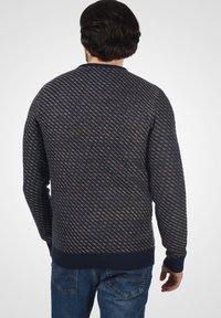 Marineblauer gestrickter Pullover mit diagonalen Mustern in Orange und Creme. Rippstrickbündchen und -saum. Die Rückansicht zeigt einen lässigen Schnitt und die Textur.