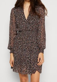 Schwarzes Blumen Kleid mit langen transparenten Ärmeln, taillierter Taille und rüschensaum. Mit V-Ausschnitt und zartem, mehrfarbigem Blumenmuster.