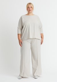 Hellgraues, leger geschnittenes Oberteil mit 3/4-Ärmeln, kombiniert mit weit geschnittenen Hosen. Glatte Textur, minimalistisches Design, keine sichtbaren Muster oder Akzente.