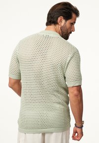 Hellgrüner, gestrickter Kurzarmpullover mit offenem Gewebe, gerippten Säumen und einem gerippten Saum. Verfügt über einen lässigen Schnitt und ein atmungsaktives Design.