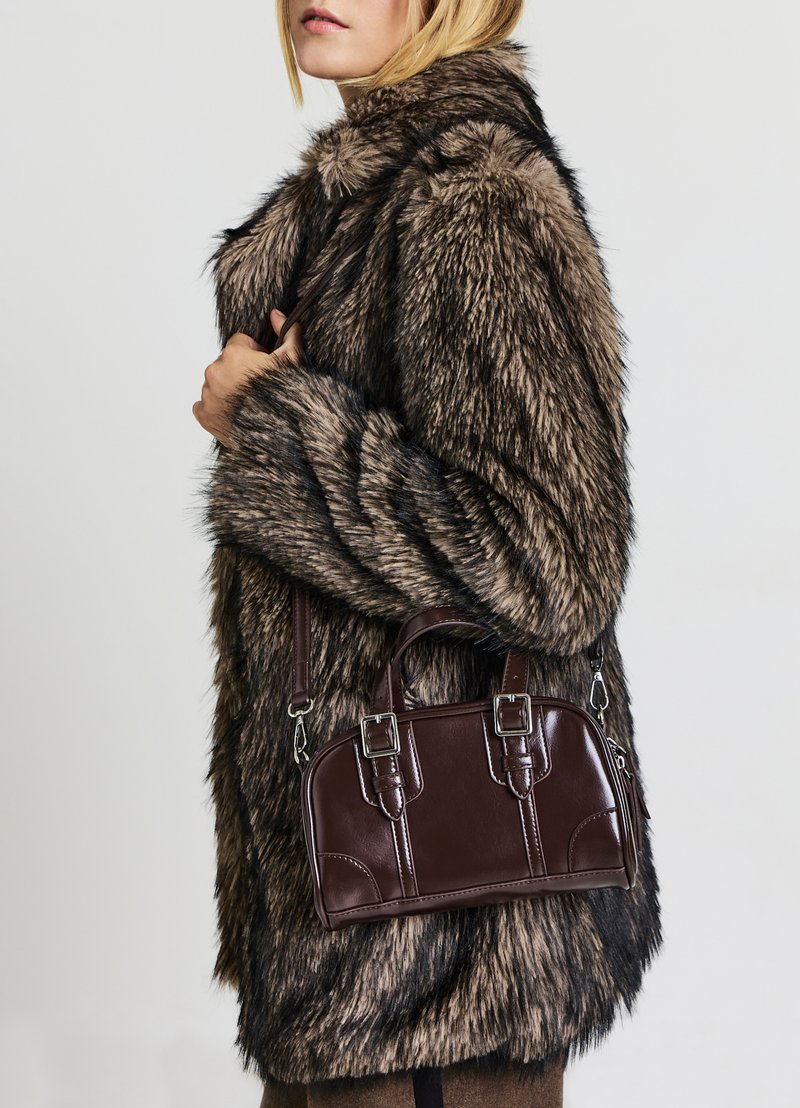 Manteau en fausse fourrure avec des rayures brunes et noires, associé à un petit sac à main en cuir synthétique marron foncé, avec des éléments en métal argenté et une bandoulière amovible.