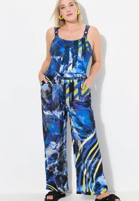 Blauwe jumpsuit met wijd uitlopende benen, voorzien van een geometrisch ontwerp in tinten blauw en groen, verstelbare bandjes en zijzakken.