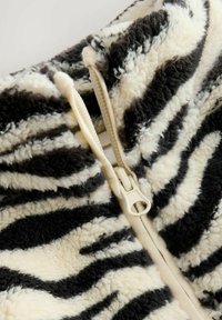 Reißverschlussjacke aus weichem, plüschigem Stoff in schwarz-weißen Zebra-Streifen; strukturierte Oberfläche mit einem weißen Reißverschluss.