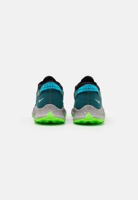 Les baskets Nike Trail Pegasus présentent une tige teal foncé, une semelle intermédiaire gris tachetée et une semelle extérieure vert fluo avec des crampons de traction.