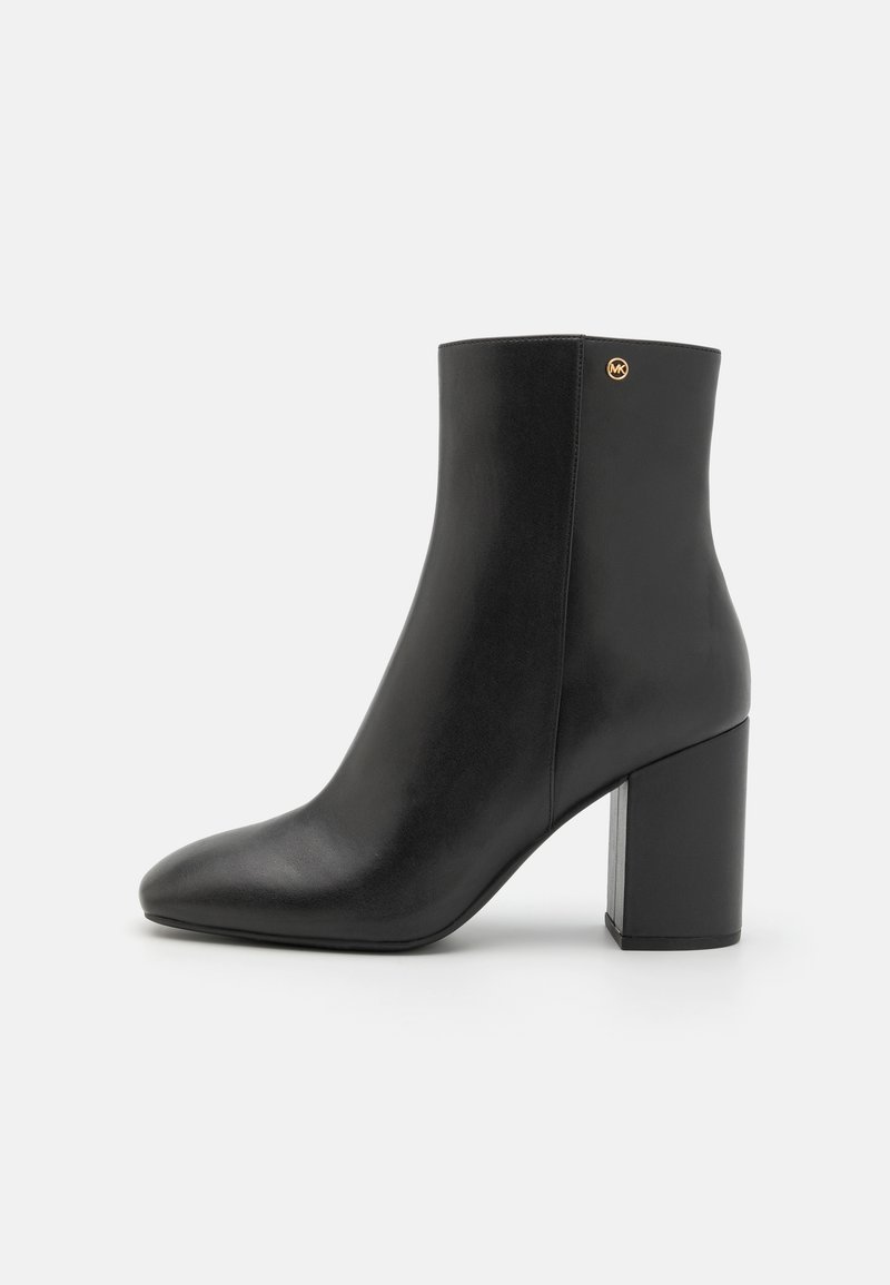 Czarne skórzane botki za kostkę z wąskim noskiem i blokowym obcasem. Posiadają mały złoty akcent z logo z tyłu. Gładka tekstura.