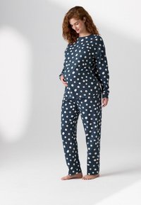 Maternity pajama set in navy blue with white polka dots; long-sleeve top and matching pants, soft texture, loose fit.