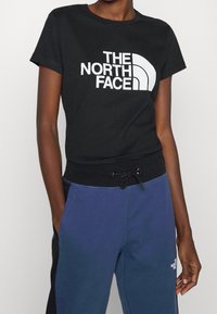 Svart bomullströja med vit logotext, korta ärmar och figurnära midja. Matchad med avslappnade blå sweatpants med dragsko.