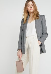 Gray plaid blazer with double-breasted design, paired with a white v-neck top and cream wide-leg pants. Holding a light pink clutch.