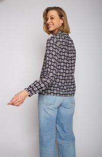 Schwarz-wei ße gemusterte Bluse mit kreisförmigen Designs, langen Ärmeln, gerafftem Ausschnitt, kombiniert mit hellblauen geraden Jeans.