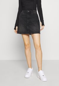 Czarna denimska spódnica w kształcie litery A z zamknięciem na guziki z przodu, dwoma kieszeniami i prostym dołem. W zestawie z białymi trampkami.