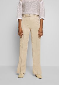 Beige wijde broek met een gestructureerde afwerking, voorzien van een riem en voornaden; gestyled met een losse, gebreide top en gevlochten schoenen.
