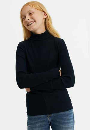 Mornarsko modra rebrasta puli majica s dolgimi rokavi, ki ima prilegajoč dizajn in udoben material, v kombinaciji z jeanskimi hlačami.