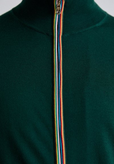 Grønn strikket genser med høy krage og frontglidelås, med flerfarget stripe detalj. Glatt tekstur, tettsittende design.