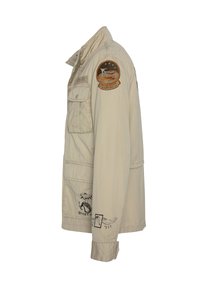 Beige militær-inspireret jakke med brystlomme, broderede patches og dekorative tryk. Har lange ærmer og krave.