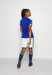 Camiseta de fútbol atlética azul de manga corta, pantalones cortos blancos y calcetines marinos con tres rayas. Diseñada para el rendimiento y la comodidad.